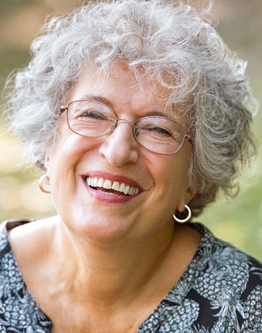 An older woman wearing glasses and smiling, showing off her new dental implants