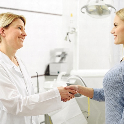 A dentist shaking hands with a female patient before her appointment