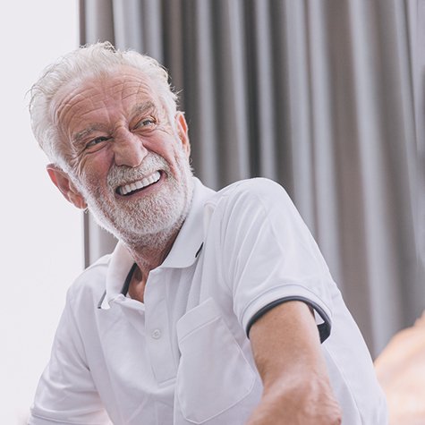 Older man wearing a white shirt and smiling with dentures