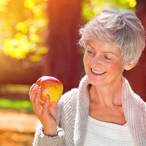 An older woman wearing a cardigan outside and holding an apple