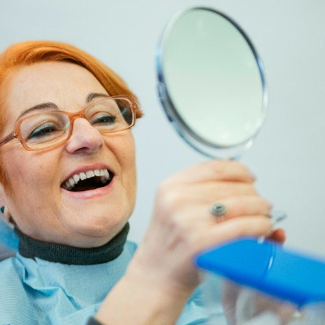 A happy woman admiring her dentures in a hand mirror