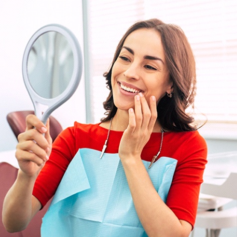 A woman wearing a red blouse admires her smile in the mirror after a regular checkup
