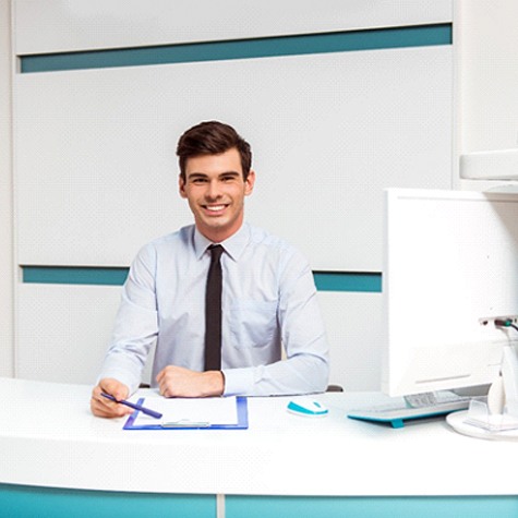 A young man sits behind the front desk of a dentist’s office in preparation to help the next patient