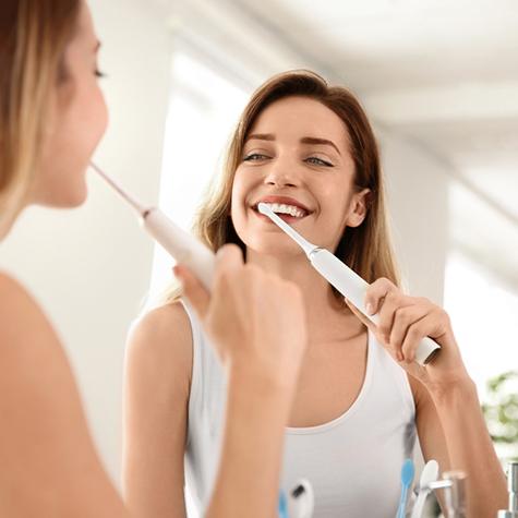A young woman using an electric toothbrush to clean her newly whitened smile